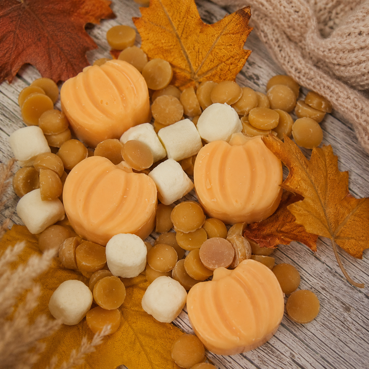 Pumpkin-shaped soap bars with white spherical soap bars on a wooden surface with autumn leaves and fabric.