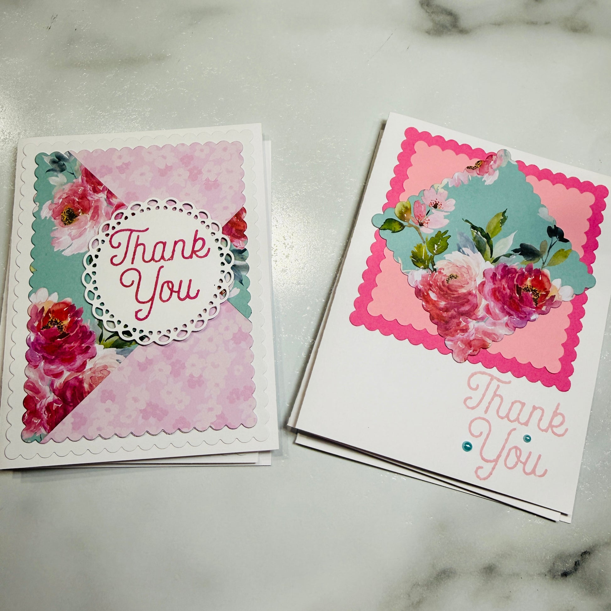 Two handmade floral thank-you cards displayed on a light marble surface. The card on the left features a pink floral pattern with a white scalloped circle containing the words 'Thank You' in pink.