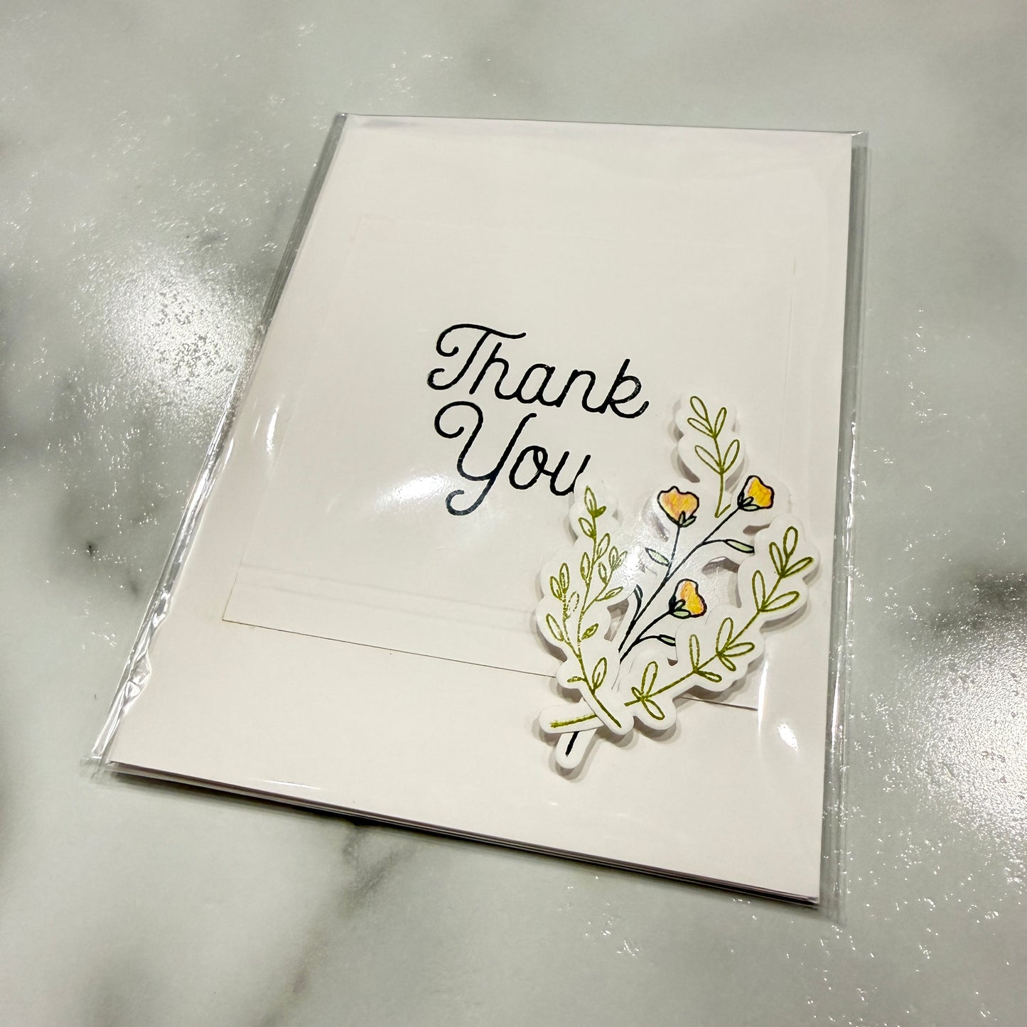 White card with 'Thank You' text and floral design on a reflective surface