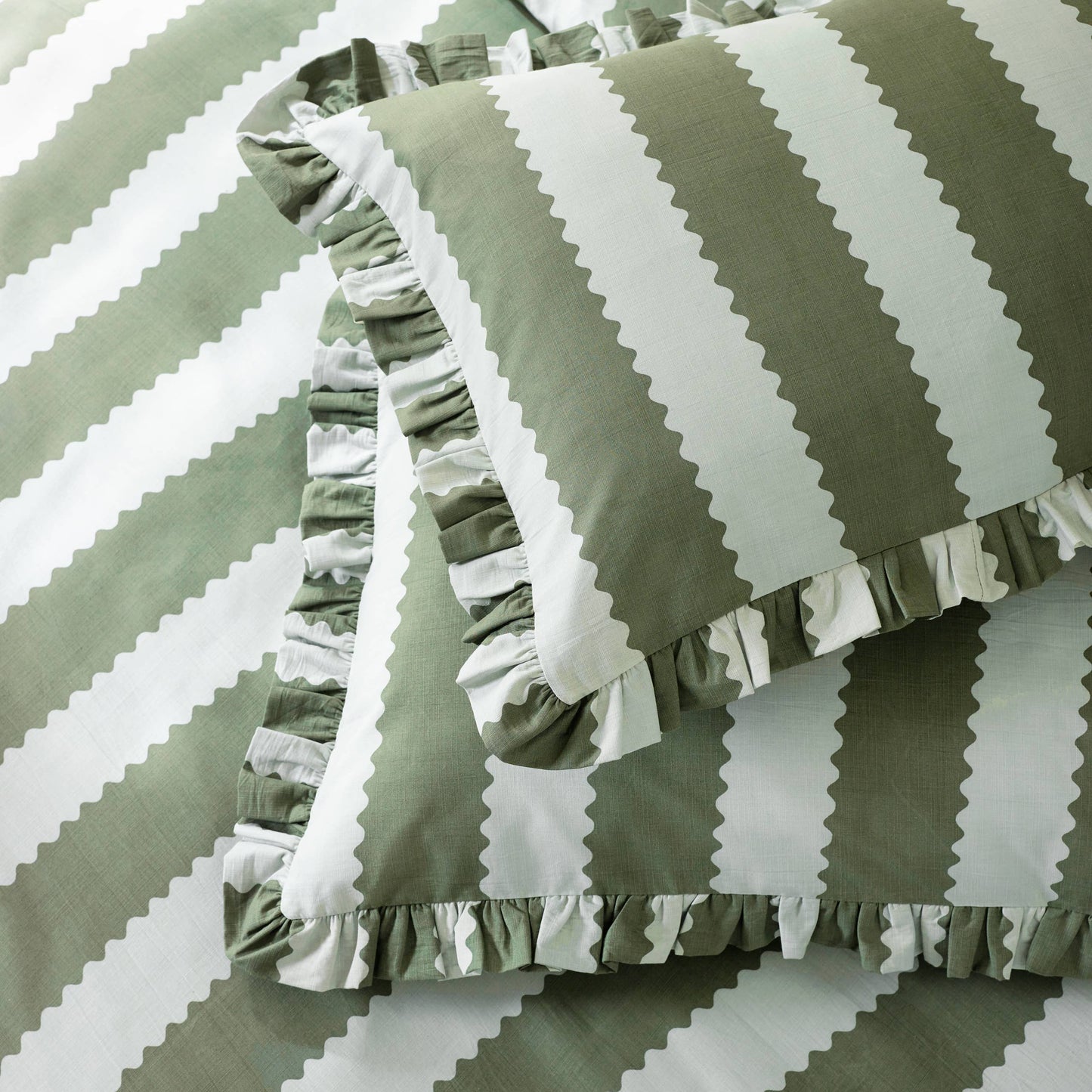 Green and white striped pillows with ruffled edges on a matching fabric background.