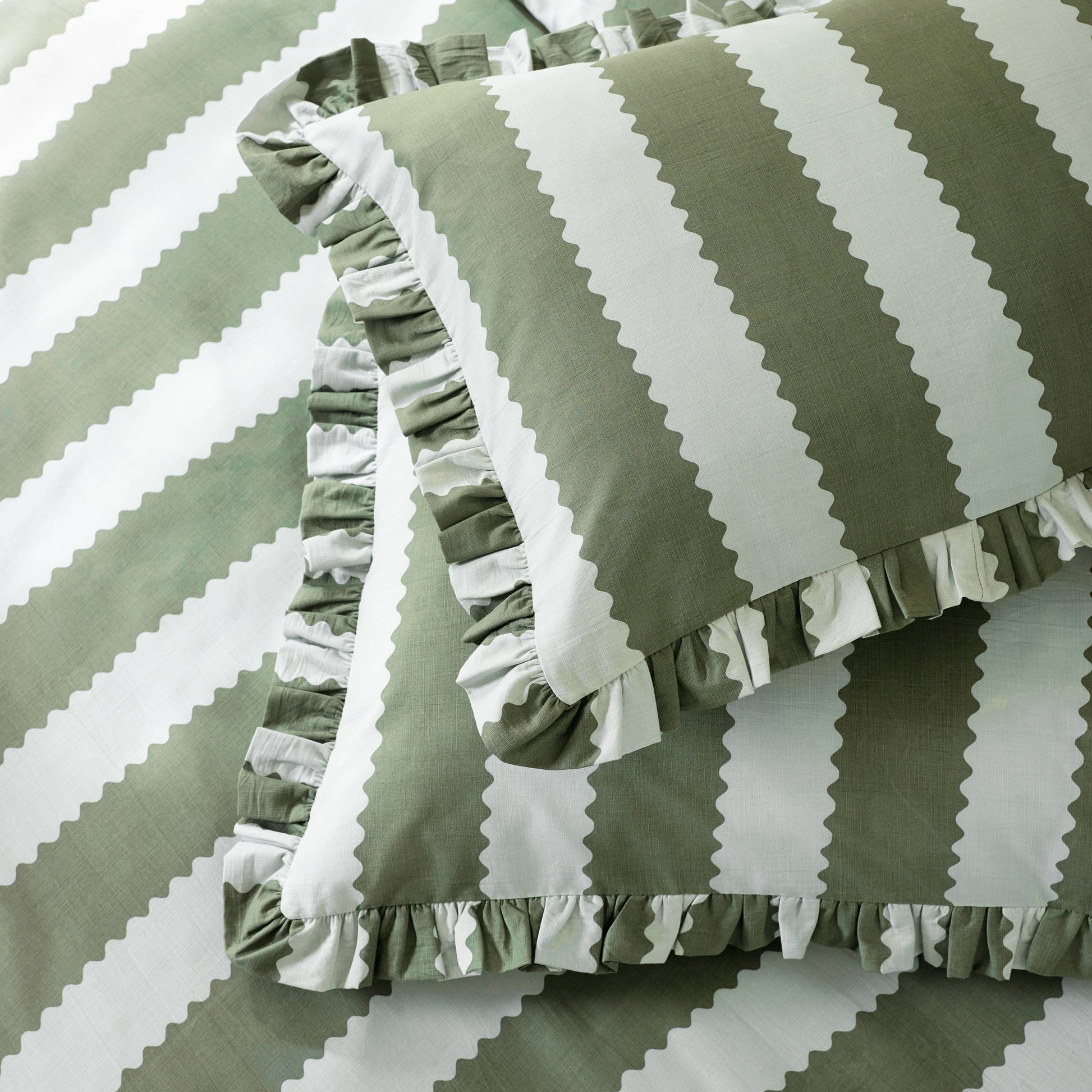 Green and white striped pillows with ruffled edges on a matching fabric background.