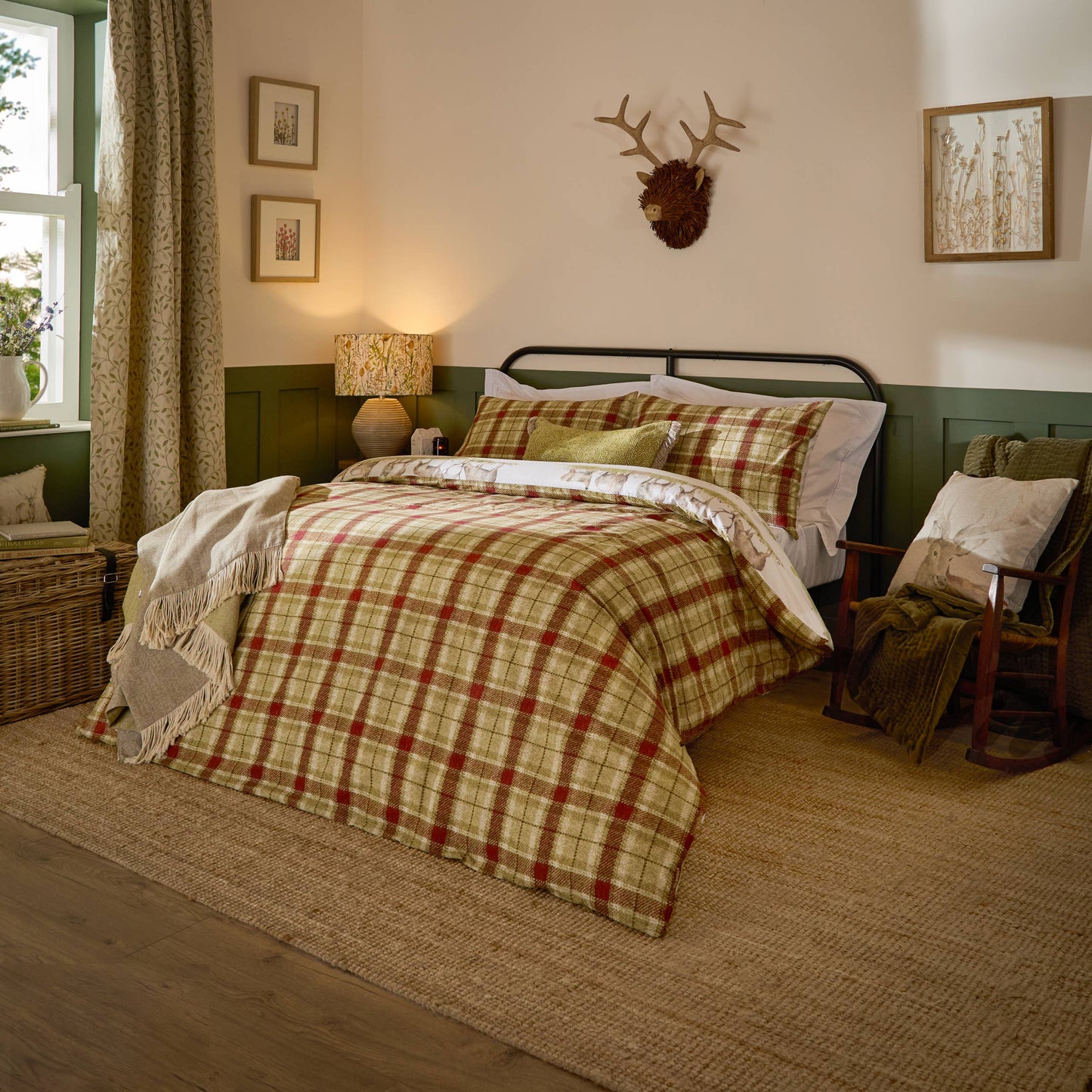 A cozy bedroom scene featuring a bed dressed in a red, green, and beige plaid comforter set, styled with matching pillows, a white throw blanket, and a rustic wooden chair beside it.