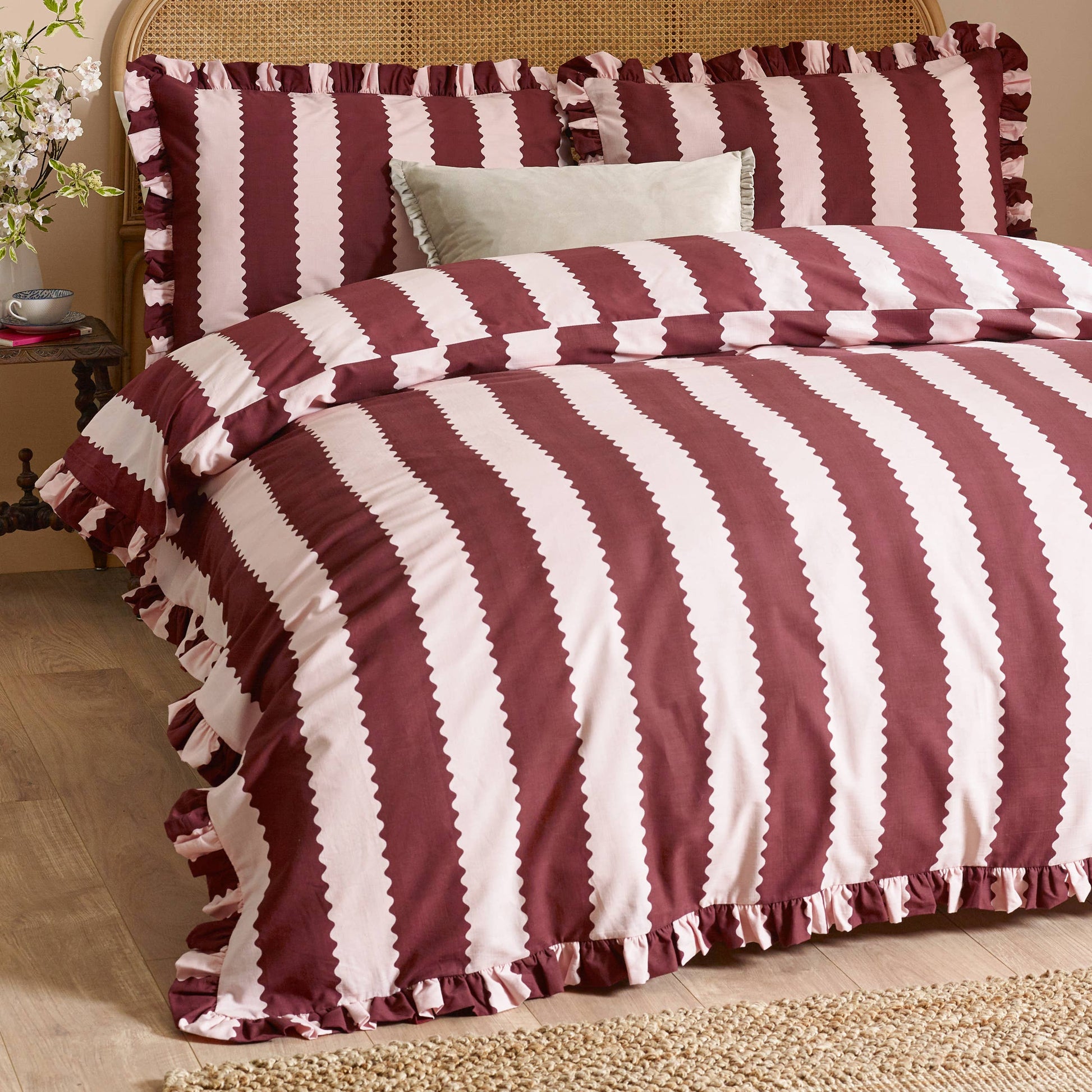 Striped burgundy and blossom comforter set on a bed with pillows.