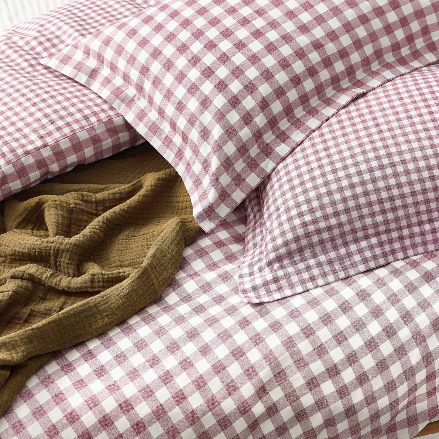 Berry and white checkered bedding with a brown blanket on a bed.