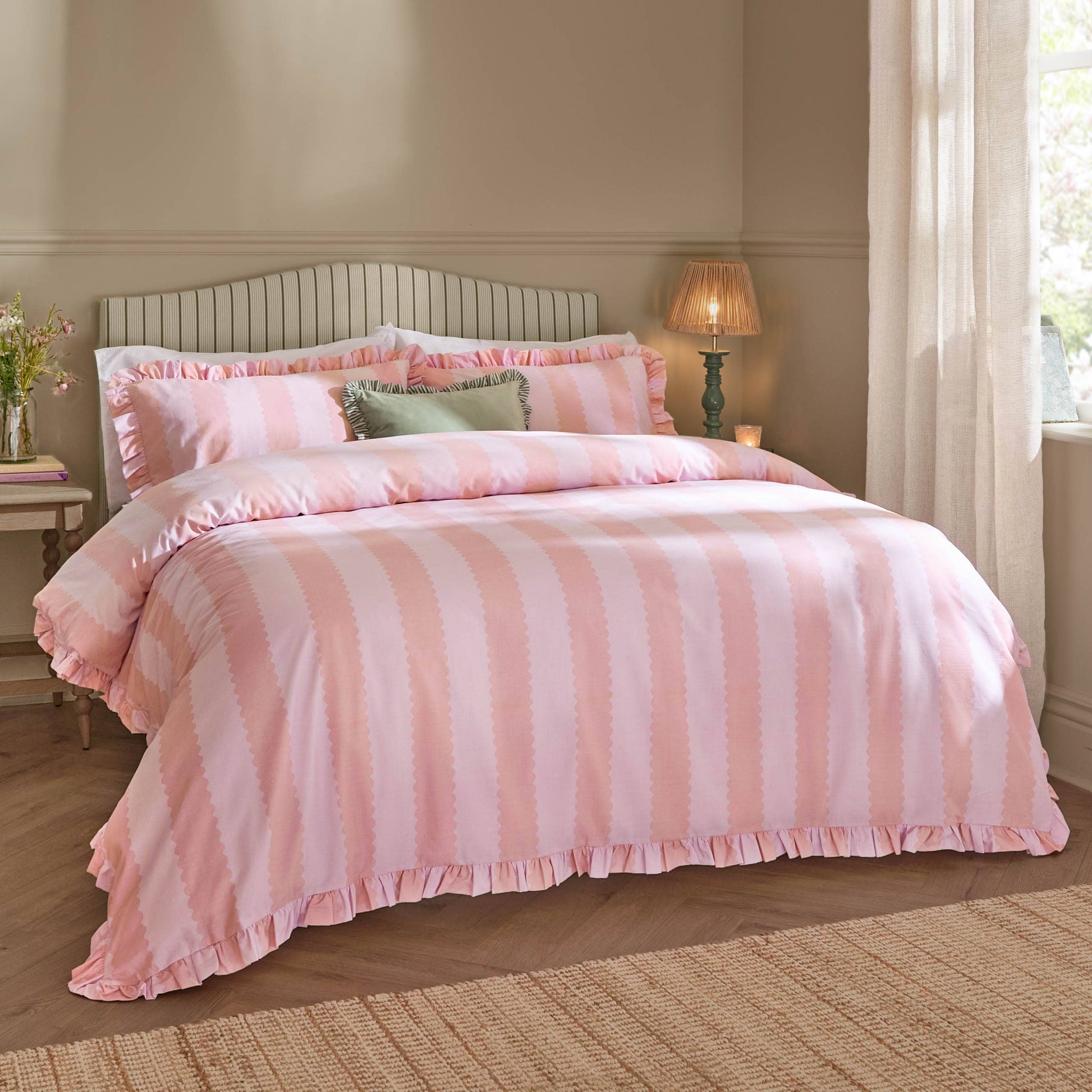 Bedroom with pink striped bedding and a lamp on a nightstand.