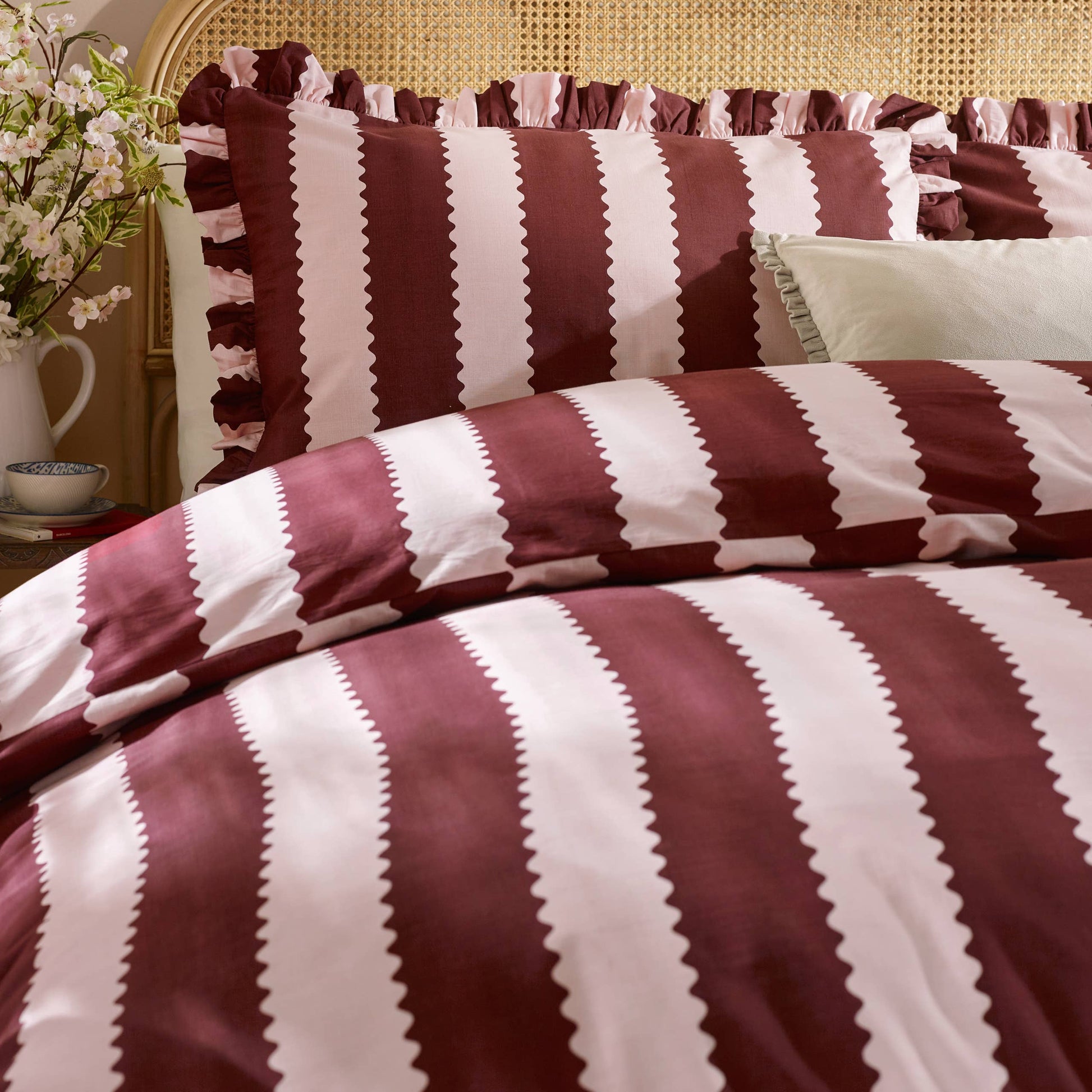 Striped bedspread with burgundy and blossom colors on a bed with pillows.