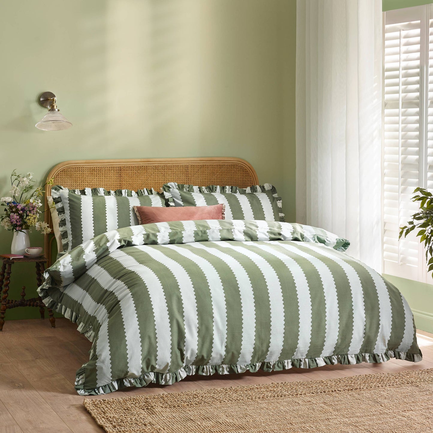 Bed with green and white striped bedding in a room with a lamp and plant.