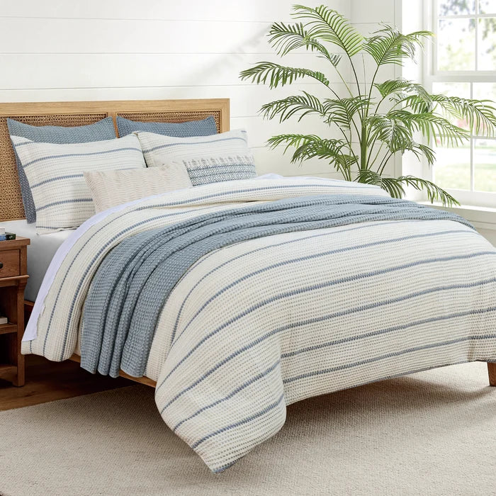 Waffle Stripe Blue Comforter Set styled with coordinating blue pillows and a textured blue throw on a natural wood and cane bed.