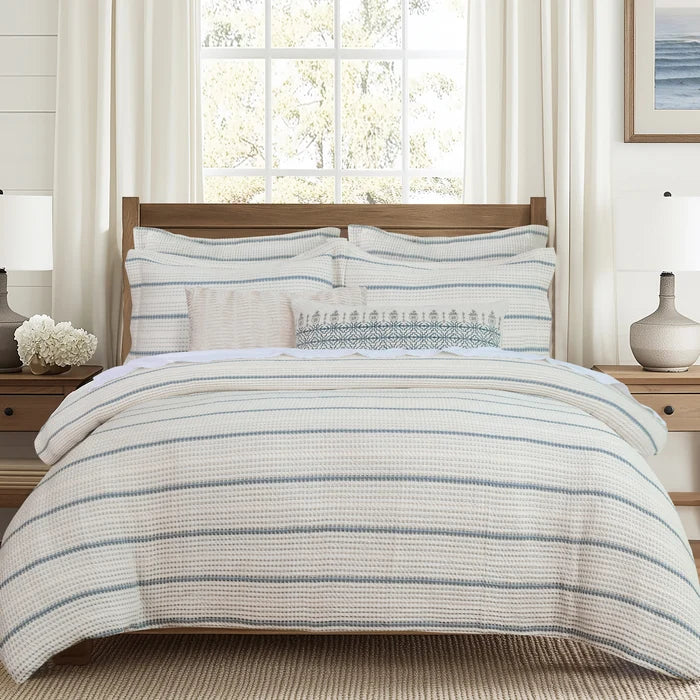Waffle Stripe Blue Comforter Set by Levtex Home featuring ivory bedding with soft blue horizontal stripes and coordinating pillow shams on a wooden bed.