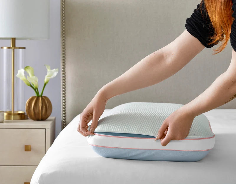 Person removing the white textured TENCEL cover from the Sleeptone Cool Control Pillow, revealing its blue cooling fabric underneath.
