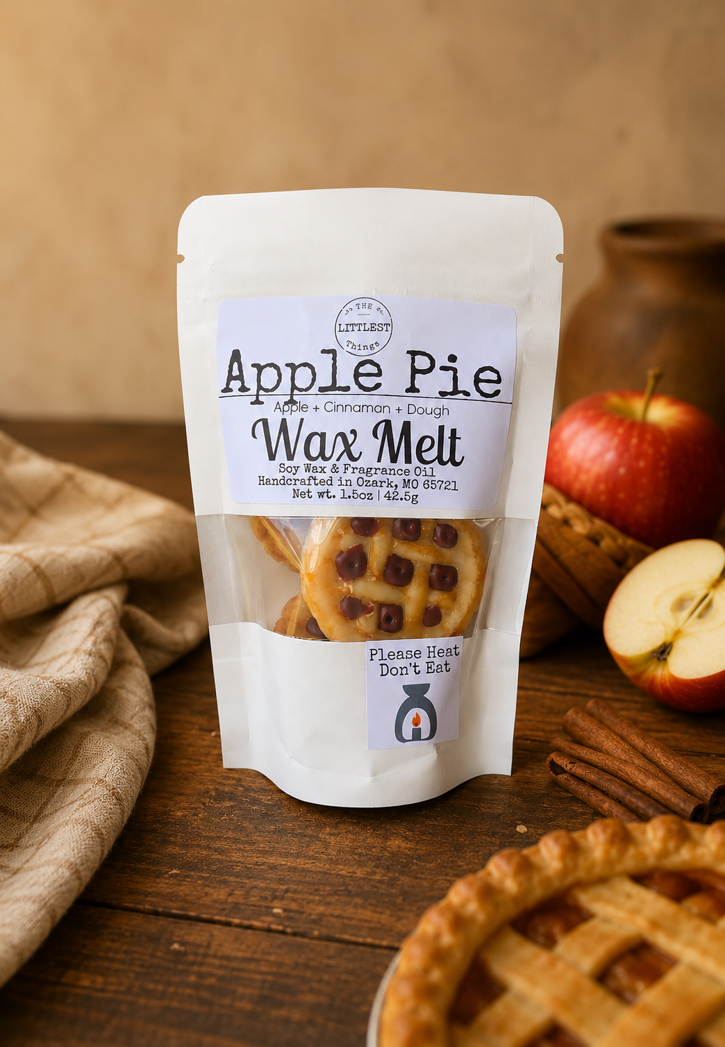 Packaged wax melt labeled 'Apple Pie' on a wooden surface with apples and cinnamon sticks.