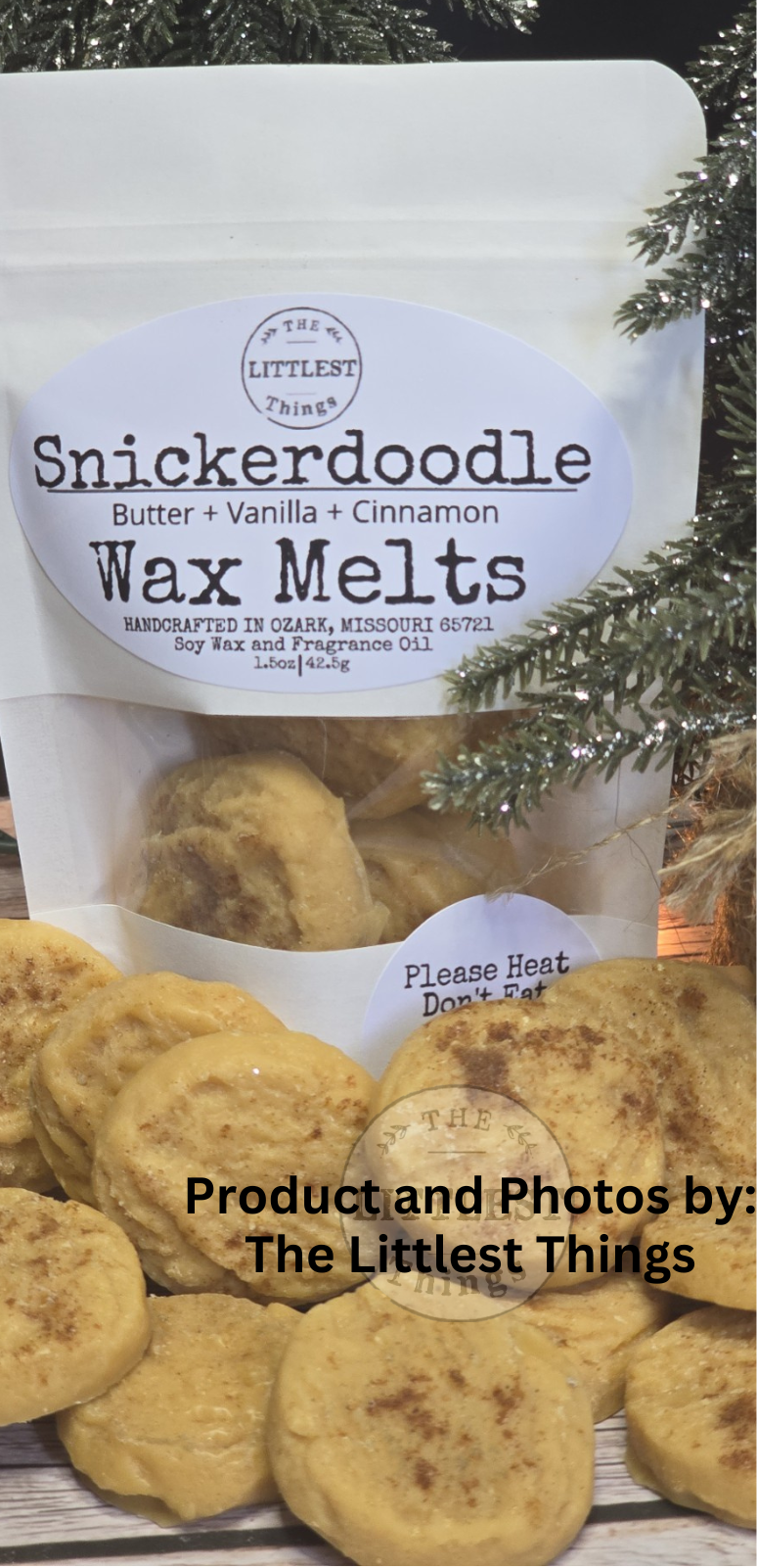 A stand-up pouch labeled 'Snickerdoodle Wax Melts' with a clear lower section showing round wax melts, placed in front of several golden-brown cookies. Pine branches frame the top and bottom, and a text overlay reads 'Product and Photos by: The Littlest Things'.
