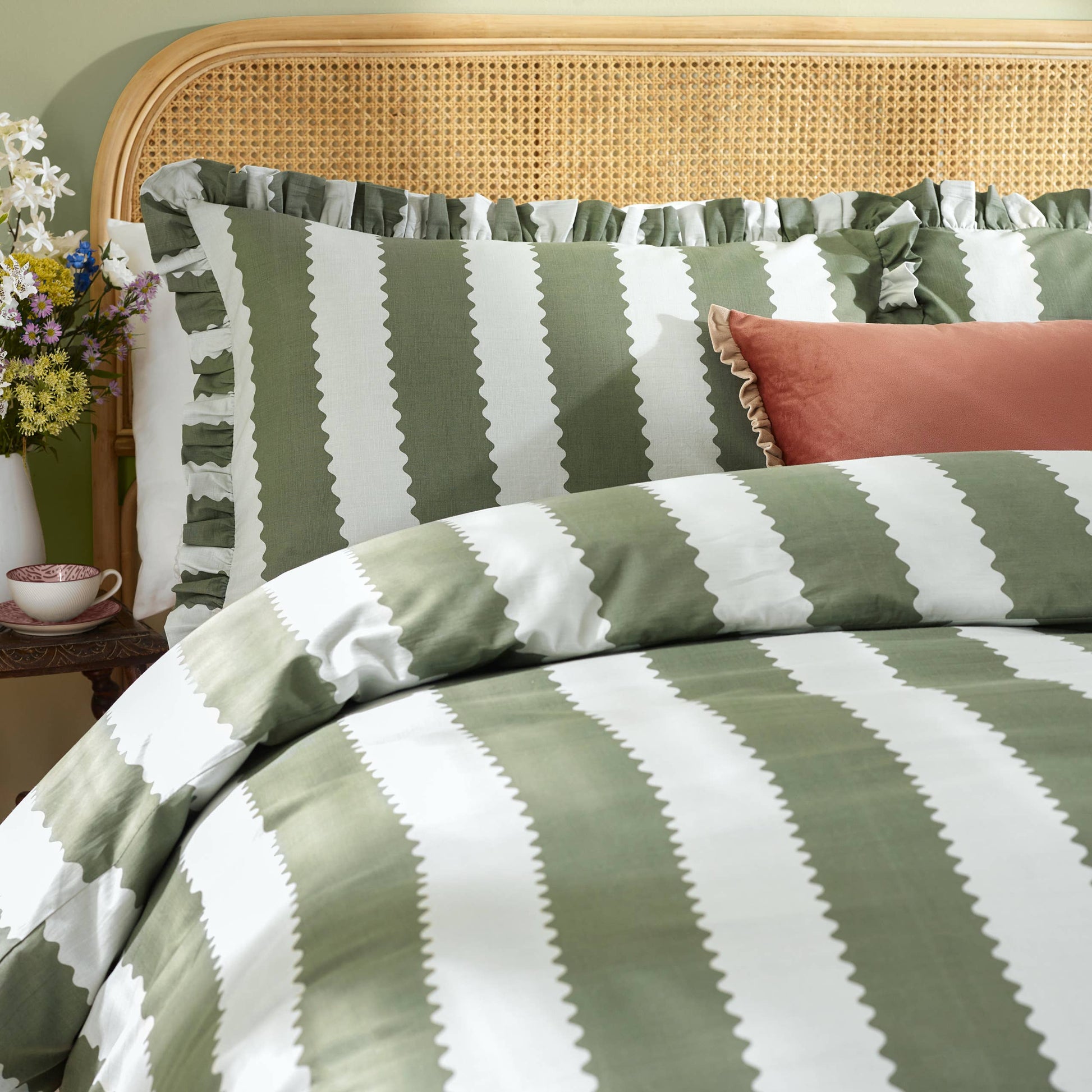 Green and white striped bedding with a wicker headboard and decorative pillows.