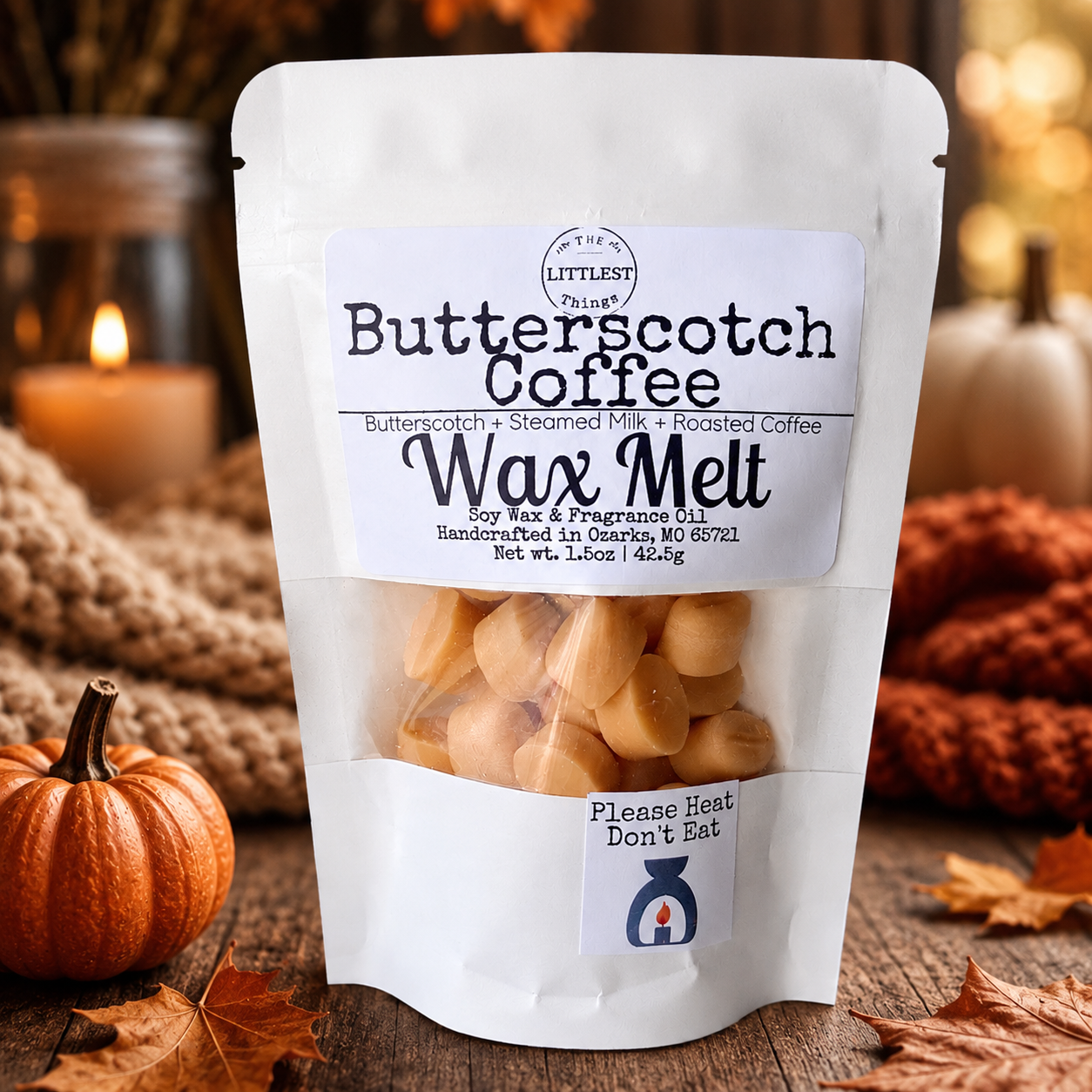 A white stand-up pouch of 'The Littlest Butterscotch Coffee' Wax Melt soy wax & fragrance oil, displayed on a rustic wooden surface with autumn leaves, a small orange pumpkin, and cozy background decor.