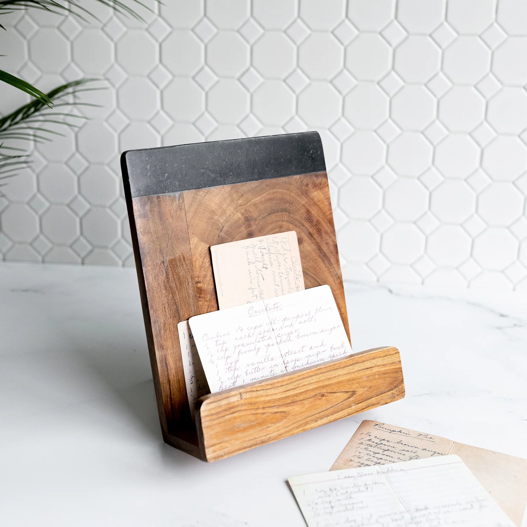 A cookbook holder made of mango wood with a solid black marble stone base, holding a cookbook and placed on a kitchen counter.